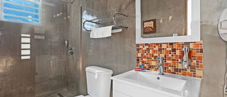 A modern bathroom with a glass-enclosed shower, a white toilet, a sink with a tiled backsplash, and a mirror above the sink.