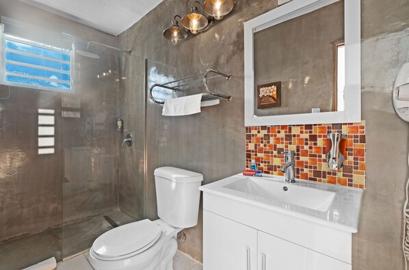 Une salle de bain moderne avec une douche à parois de verre, des toilettes blanches, un lavabo avec un pare-éclaboussures carrelé et un miroir au-dessus du lavabo.