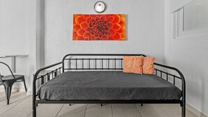 A bed with a metal frame, a grey patterned mattress, and two pillows, one orange and one white.