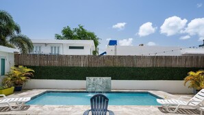 A swimming pool with a waterfall feature, surrounded by a wooden fence and potted plants.