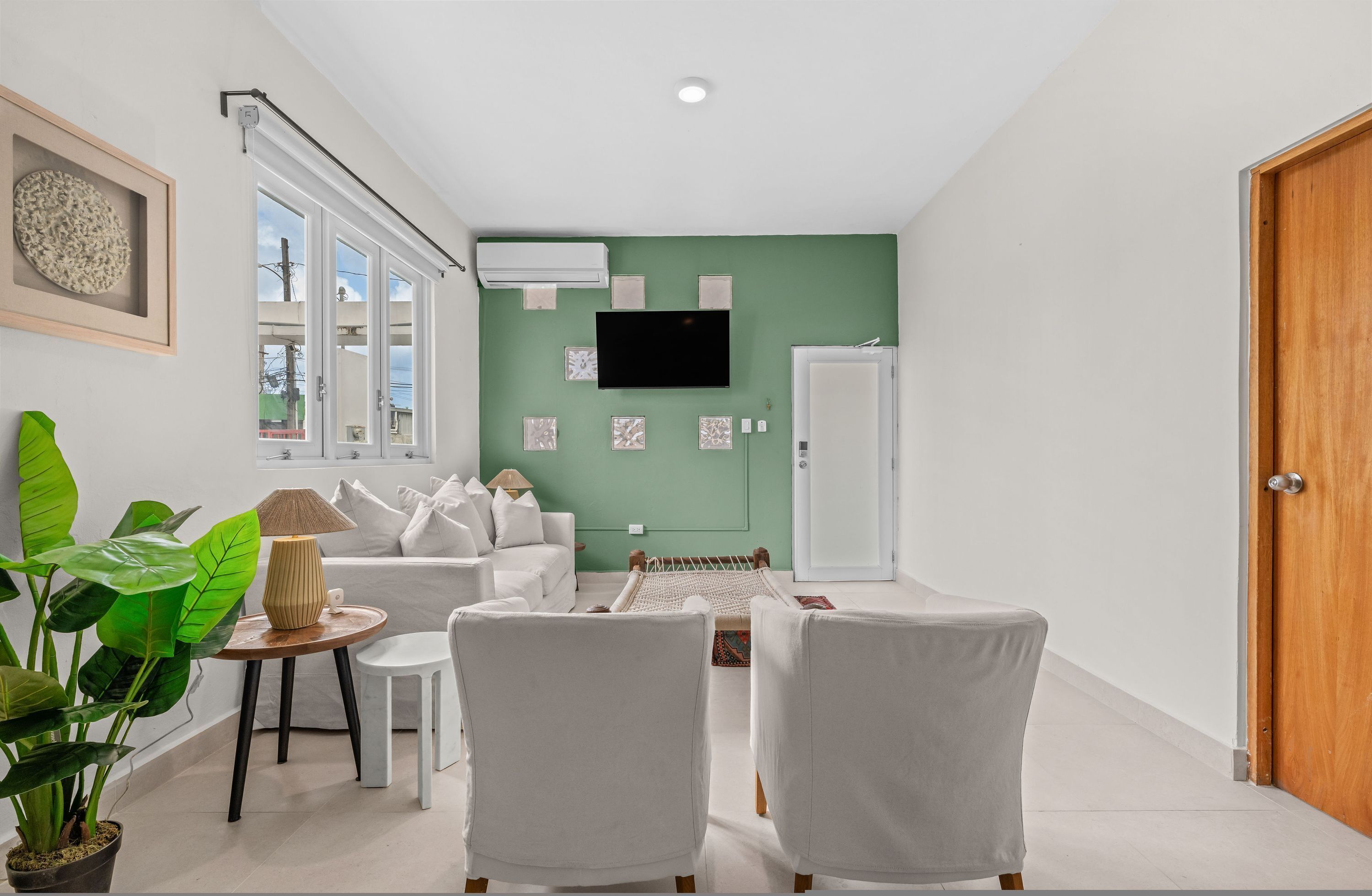 En moderne stue med en hvid sofa, to hvide lænestole, et lille bord med en lampe og en stor, grøn væg.