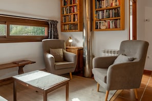 Un salon chaleureux avec une cheminée, deux fauteuils, une table en bois et des étagères remplies de livres.