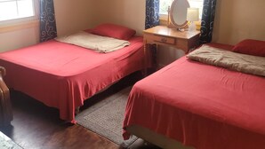 A room with two beds, a ceiling fan, a window with curtains, a bedside table with a lamp, and a small table with a chair. - House can sleep 8 or more people (Aliquippa)