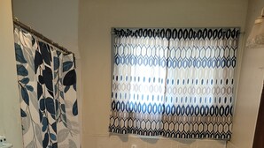 A small bathroom with a shower curtain, a toilet, a sink, and a window with patterned curtains. - House can sleep 8 or more people (Aliquippa)