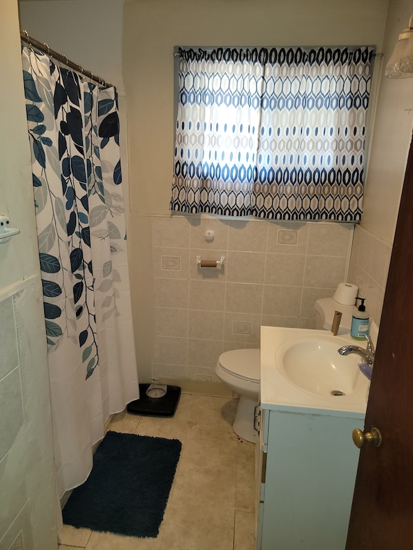 A small bathroom with a shower curtain, a toilet, a sink, and a window with patterned curtains.