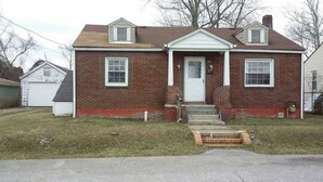 A two-story brick house with a white front door, a small porch, and a garage. - House can sleep 8 or more people (Aliquippa)