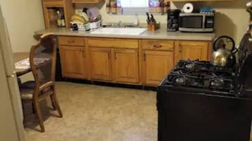 A kitchen with wooden cabinets, a stove, a microwave, and a window with curtains.