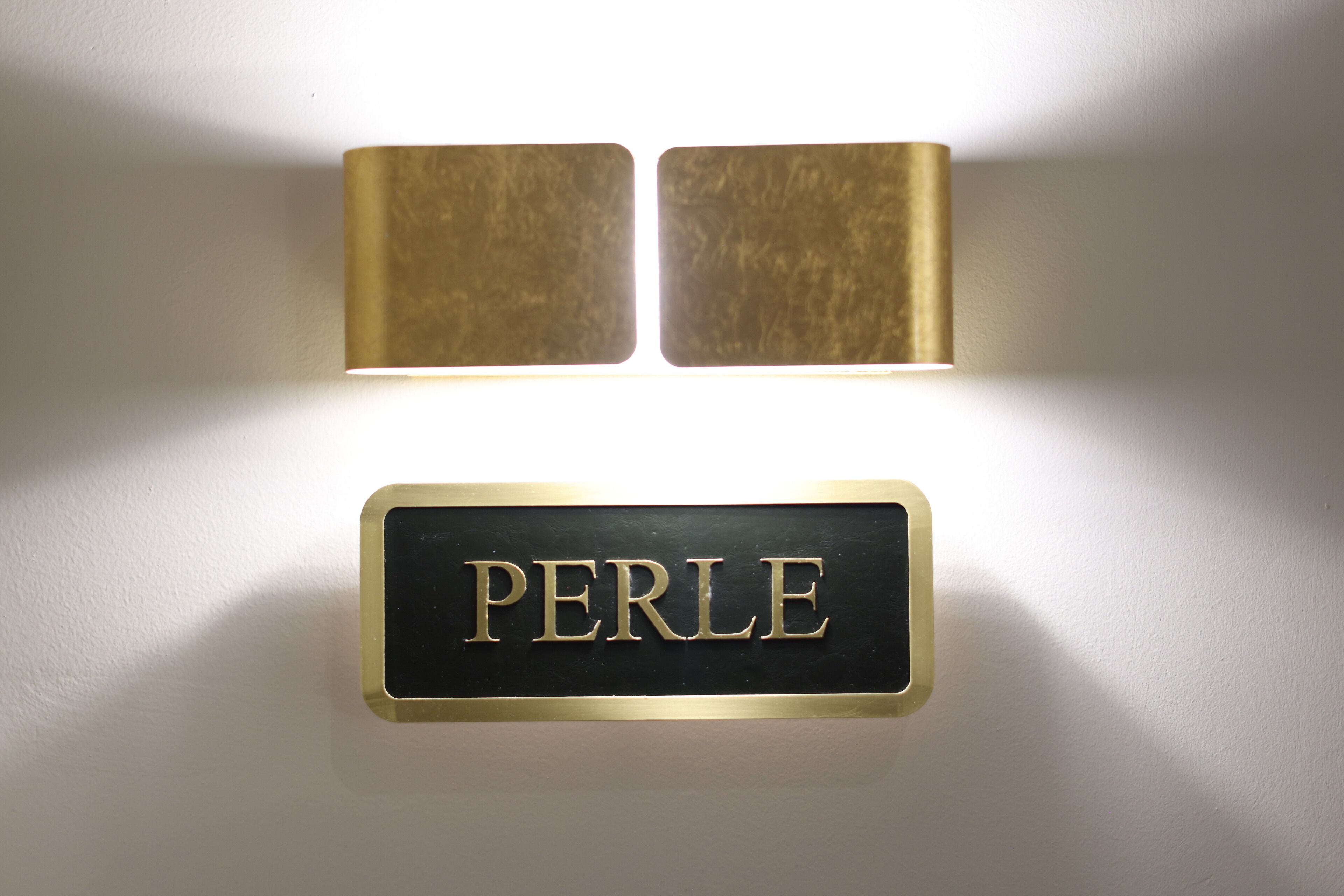Une enseigne fixée au mur, portant le nom « PERLE » en lettres de couleur dorée.