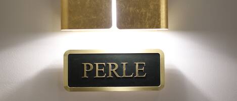 Une enseigne fixée au mur, portant le nom « PERLE » en lettres de couleur dorée.