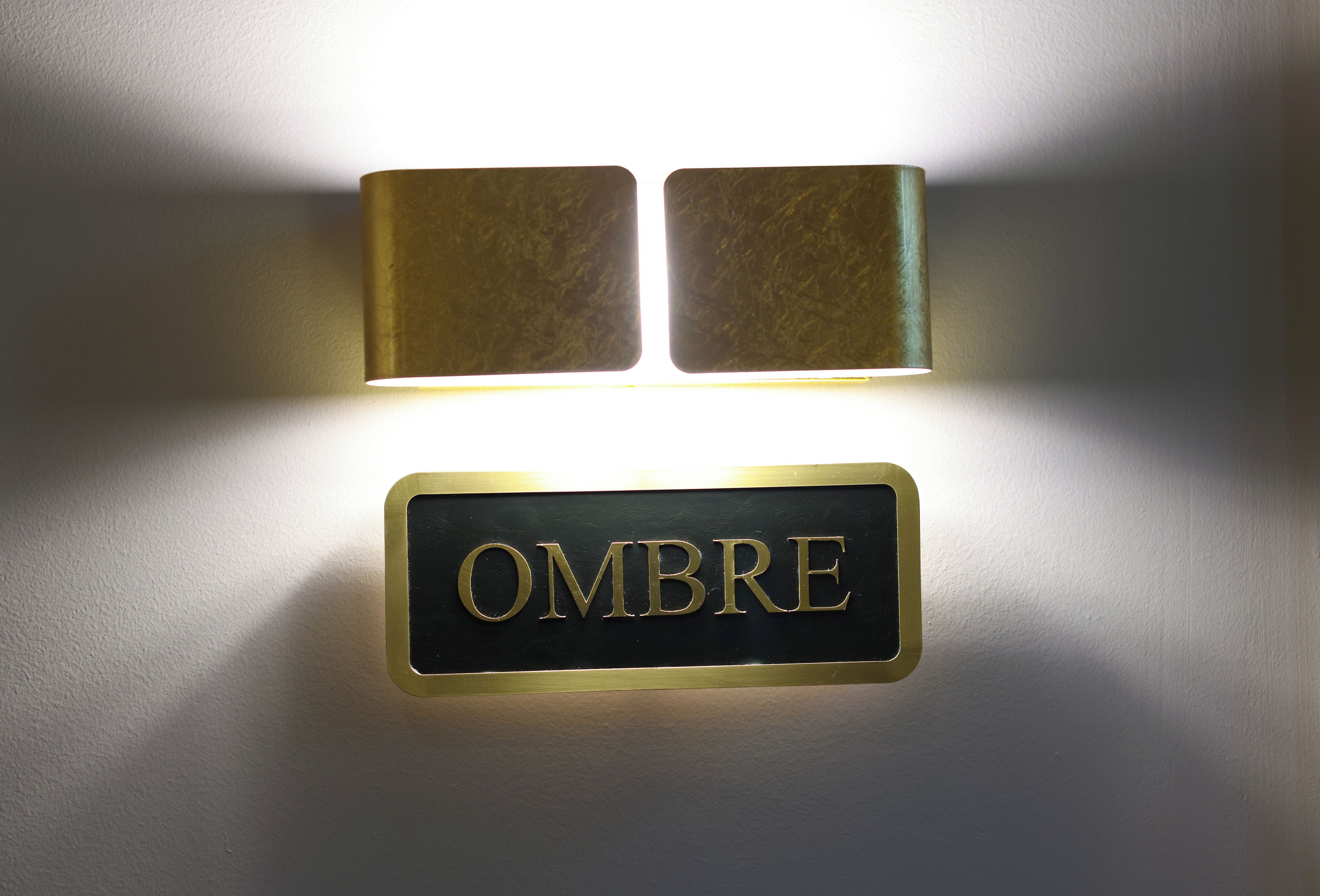 A wall-mounted sign with the word "OMBRE" in gold lettering on a black background.