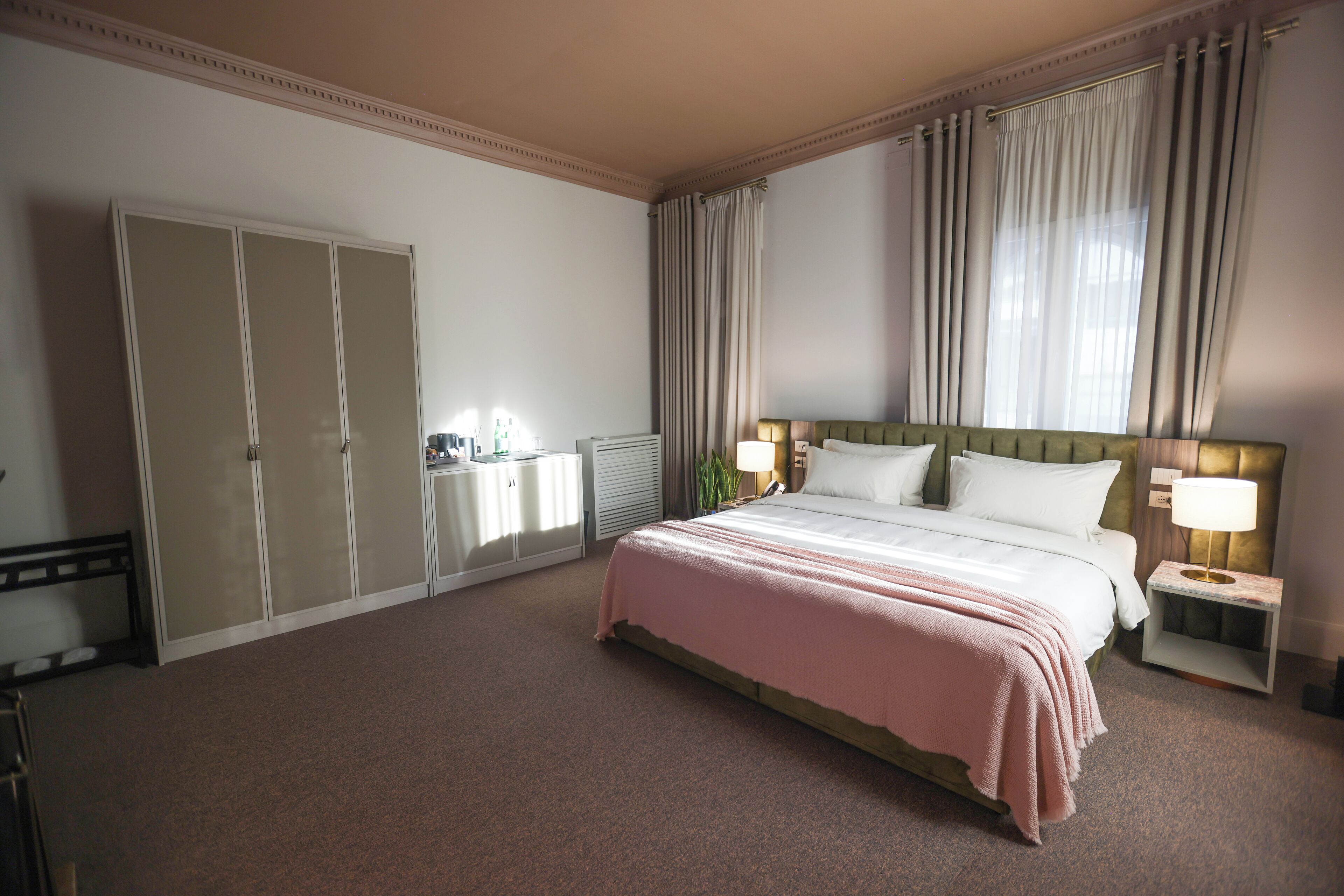 Et hotelværelse med en stor seng, et natbord med lampe, et garderobeskab og en radiator.