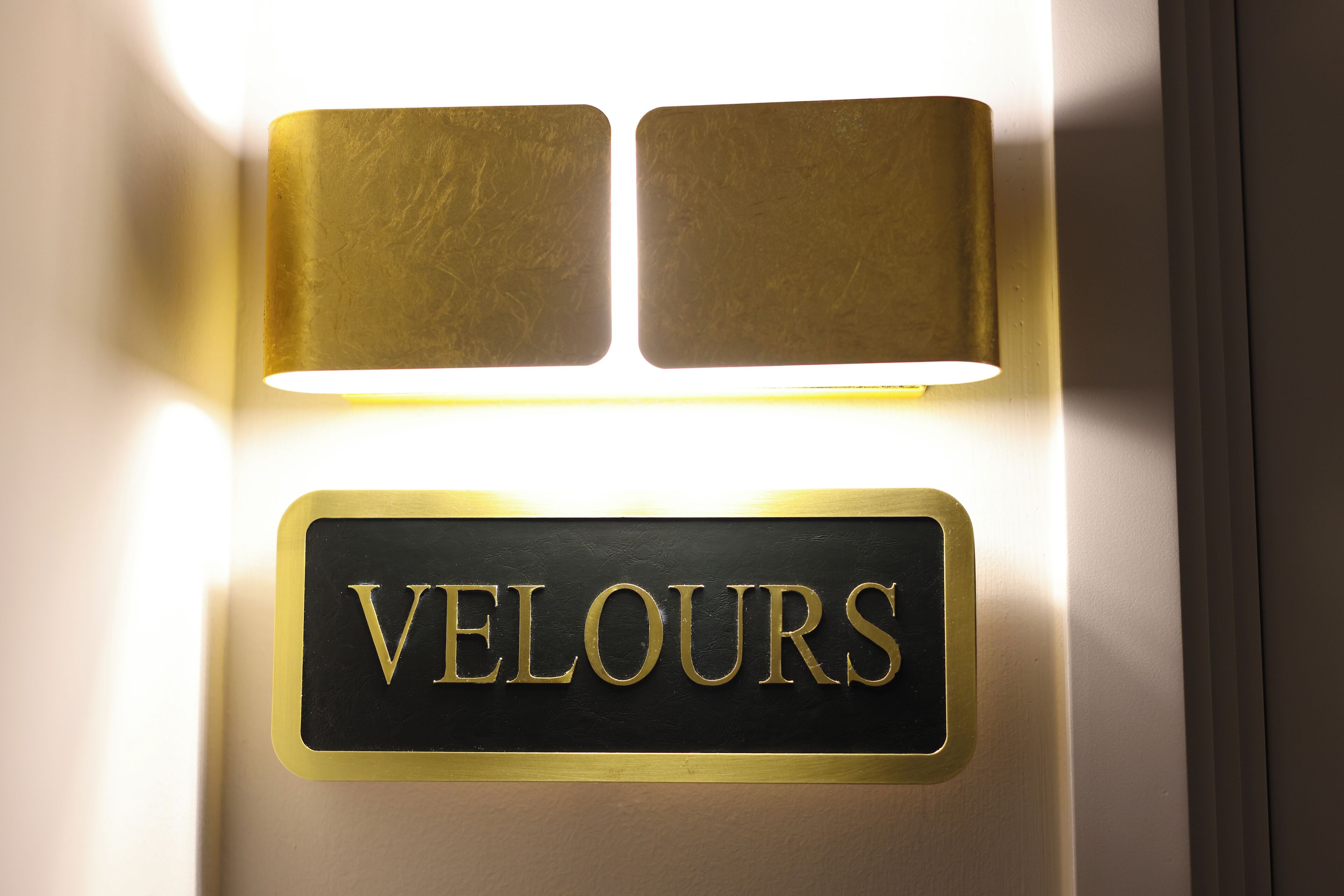 A wall-mounted sign with the name "VELOURS" in gold lettering on a black background.