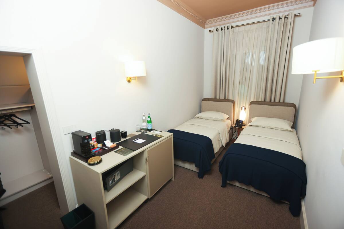 A hotel room with two single beds, a desk with a computer, a telephone, and a small trash bin.