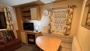 Interni di un camper compatto con divano, un tavolino, televisione e orologio a parete.