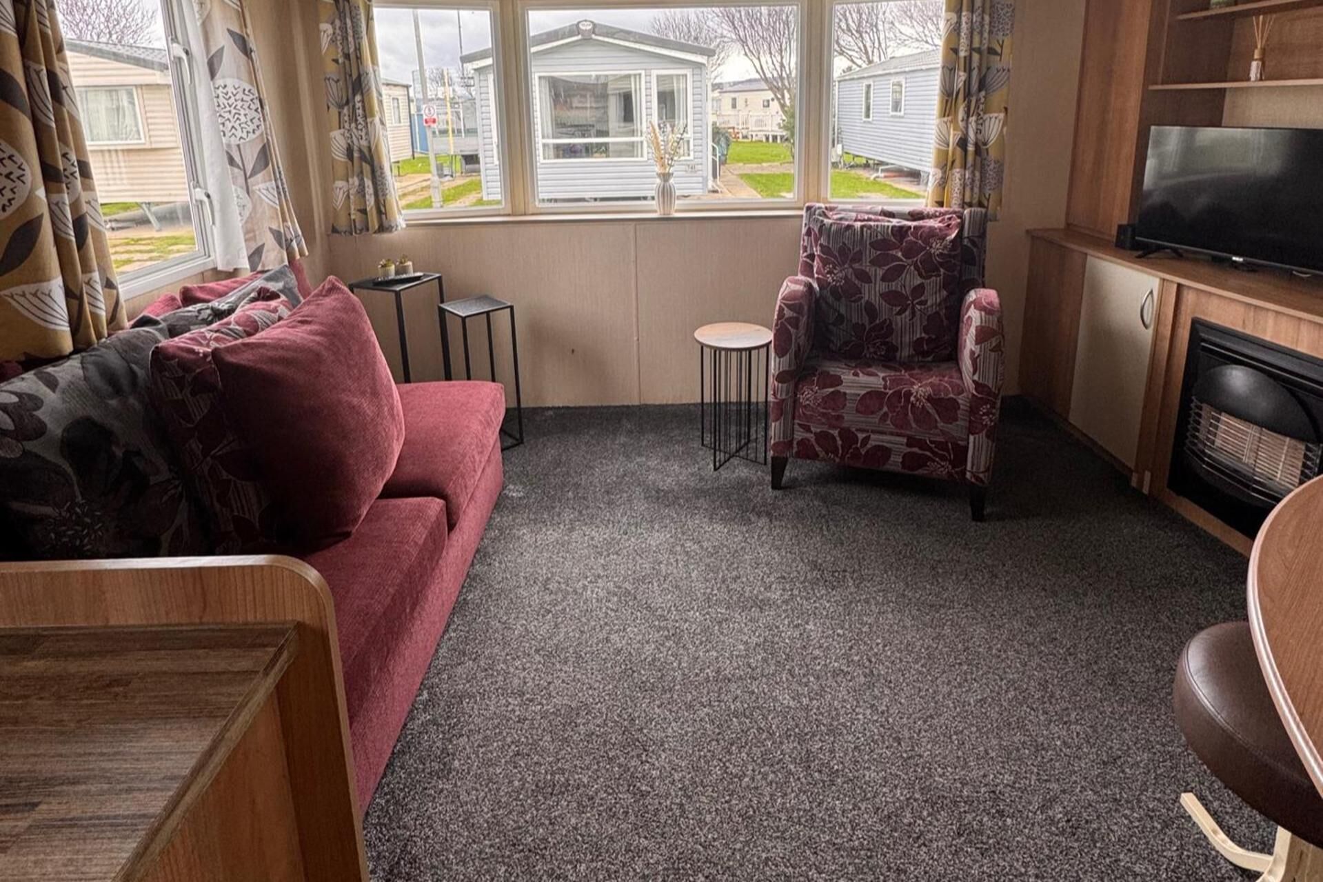 Una sala de estar con sofá, un sillón estampado, una mesita redonda y un televisor.