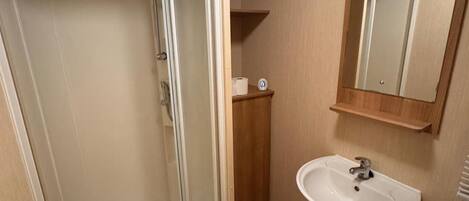 A bathroom with a glass shower enclosure, a white sink, and a mirror above the sink.