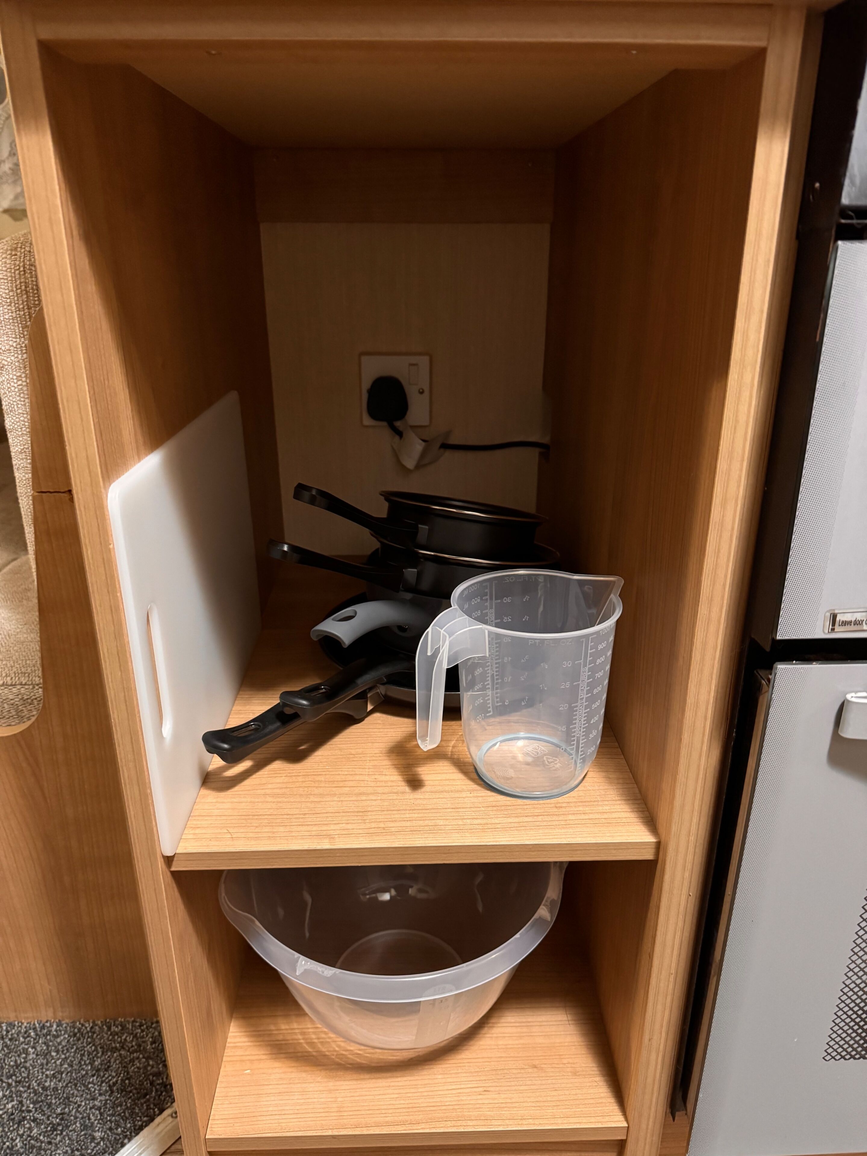 A small kitchen area with a white refrigerator, a black frying pan, a measuring cup, and a large plastic bowl.