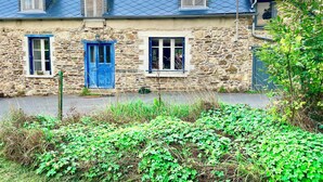 A stone house with a blue roof, two windows with shutters, and a blue door.