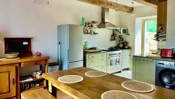 A kitchen with a wooden table, a refrigerator, an oven, and a washing machine.