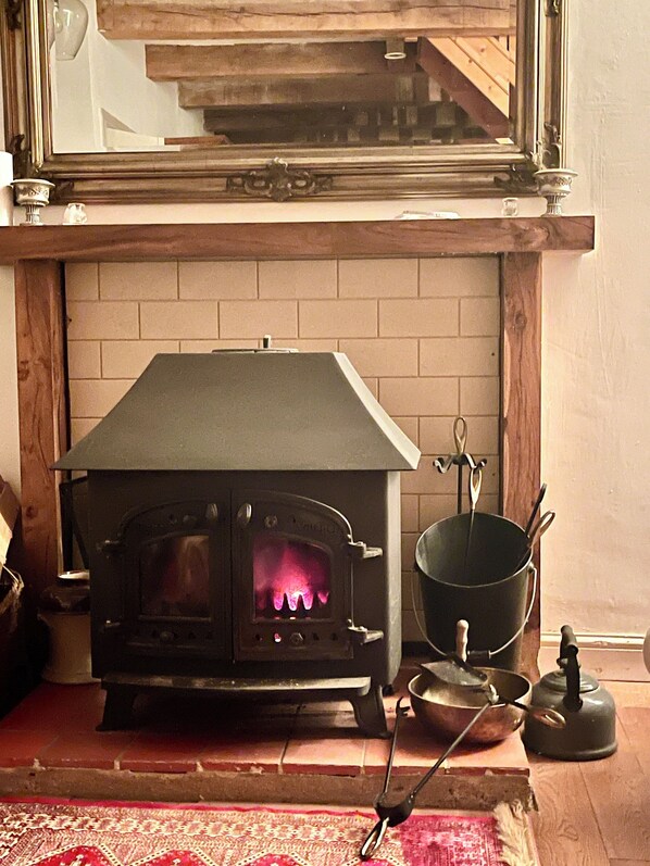 A wood-burning stove with a brick fireplace, a kettle, and cooking utensils.