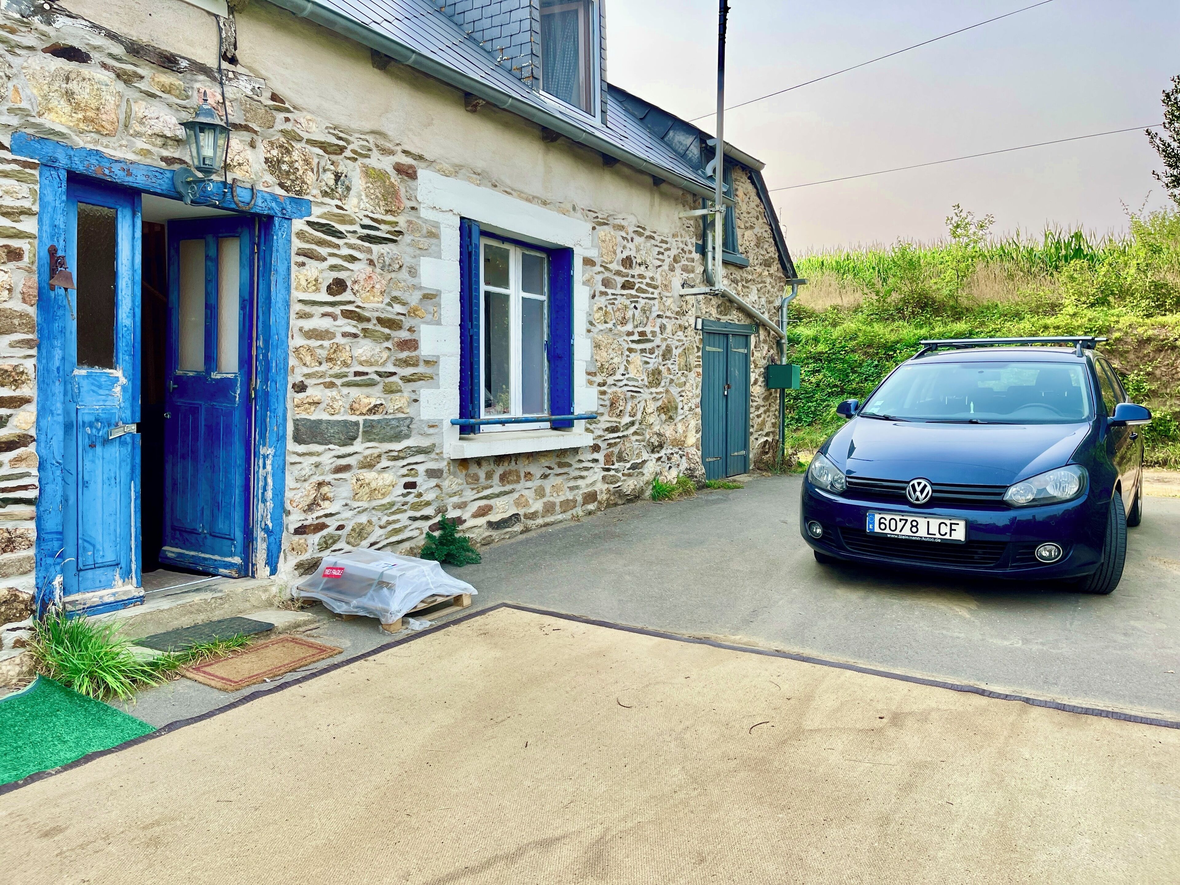 Een stenen huis met blauwe deuren en ramen, een geparkeerde auto en een smalle oprit.