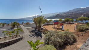 A coastal walkway with palm trees, a red kiosk, and a view of the sea and mountains. - Vacation Apartment 'Paraíso Atlántico' with Sea View, Wi-Fi & Air Conditioning (Radazul)