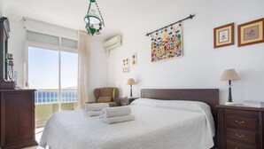 A hotel room with a large bed, a chair, a nightstand, a lamp, a dresser, a balcony with a view, and a wall with framed pictures. - Vacation Apartment 'Paraíso Atlántico' with Sea View, Wi-Fi & Air Conditioning (Radazul)