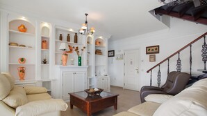 A living room with a sofa, armchair, and a coffee table. There are shelves with decorative items and a chandelier. A staircase is visible in the background. - Vacation Apartment 'Paraíso Atlántico' with Sea View, Wi-Fi & Air Conditioning (Radazul)
