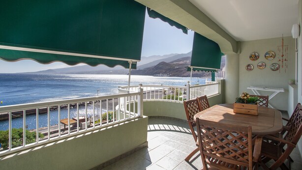 A balcony with a view of the sea, a wooden table with chairs, and a small plant on the table. - Vacation Apartment 'Paraíso Atlántico' with Sea View, Wi-Fi & Air Conditioning (Radazul)