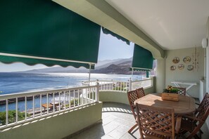 Un balcon avec vue sur la mer, une table en bois avec des chaises et une petite plante posée sur la table.