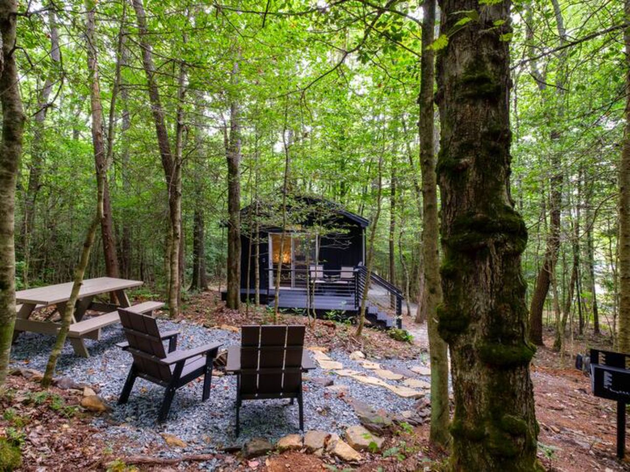 A forest cabin with a deck, picnic tables, and benches.