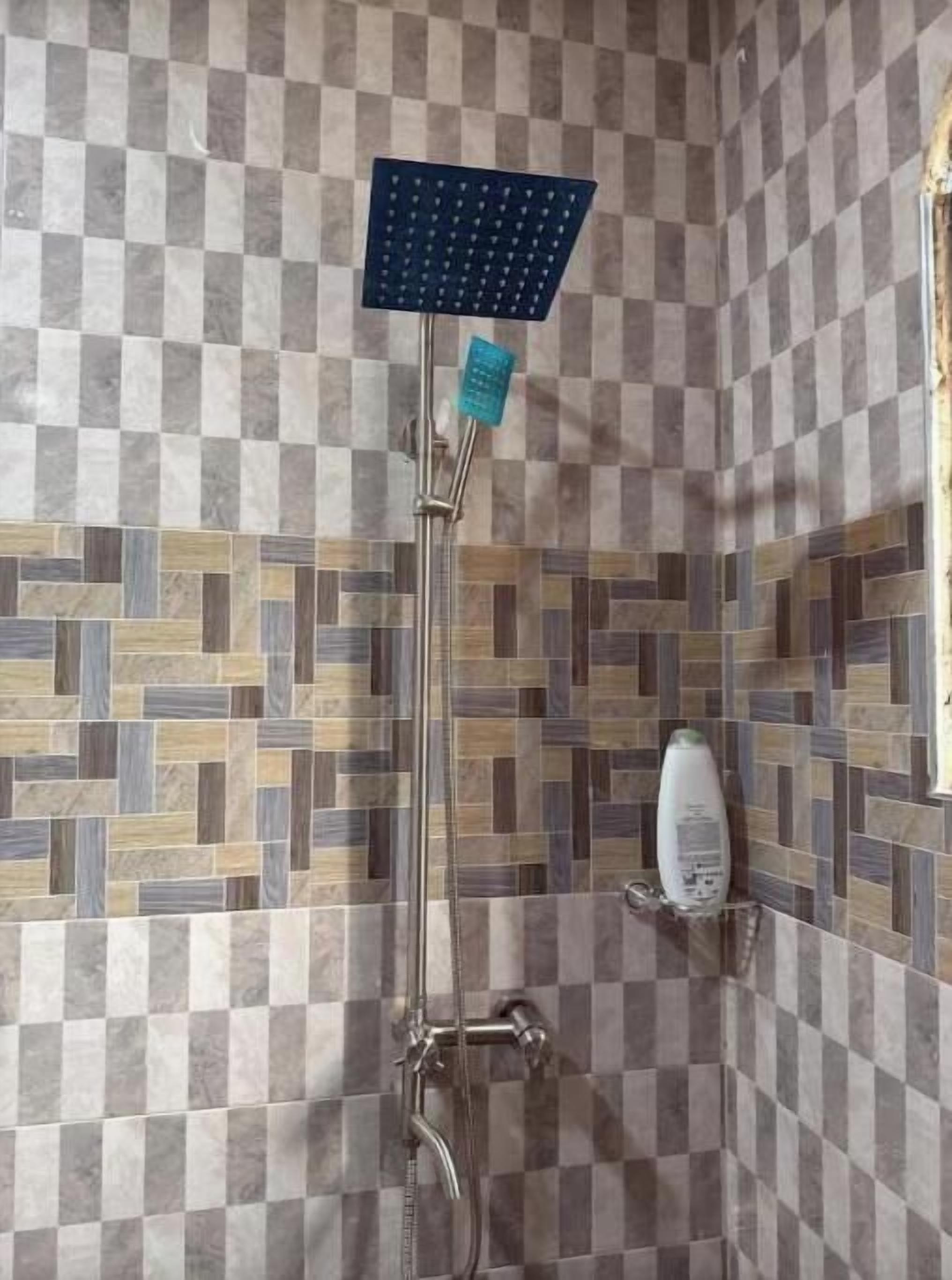 A shower with a square head, a handheld showerhead, and a soap dispenser on the wall.