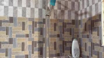 A shower with a square head, a handheld showerhead, and a soap dispenser on the wall.