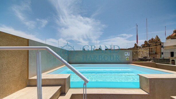 Una piscina con vistas a un edificio histórico que dice "GRAND HARBOUR".