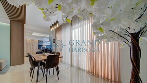 Un comedor moderno con una mesa y sillas de madera, una cocina al fondo y un árbol decorativo con flores blancas.