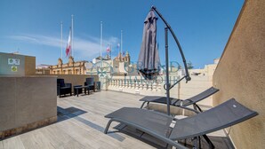 En takterrass med solstolar och ett bord, med utsikt över en historisk byggnad prydd med flaggor.