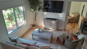 A spacious living room with a large window, a flat-screen TV, a wooden coffee table, and a sofa with cushions. - Bright & Stylish Home Stay Minutes from Wineries (Petaluma)