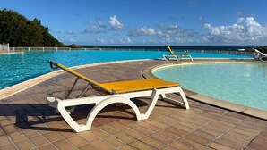 A poolside area with a curved pool, a single lounge chair, and a view of the ocean.