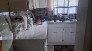 A kitchen with white cabinets, a tiled backsplash, a window with floral curtains, and a sink.