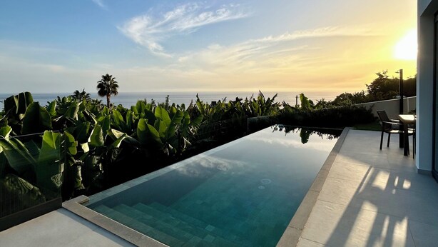 Una piscina moderna al aire libre con vistas despejadas al océano y un atardecer de fondo.