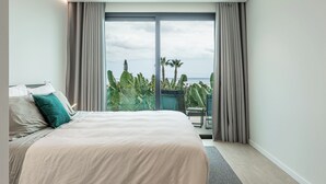 Habitación de hotel moderna con una cama grande, un balcón y vistas a palmeras y un cielo nublado.