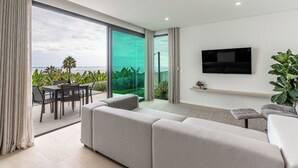 Una sala de estar moderna con un sofá grande, un televisor de pantalla plana y vistas al océano a través de amplios ventanales.