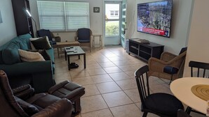 A living room with a sofa, chairs, a coffee table, a TV, and a door leading outside. - Amazing move in ready condo just 10 minutes from the beach. 65 plus community. (St Petersburg)