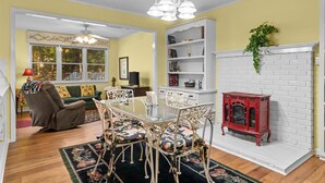 Un coin repas avec une table en verre et des chaises à motifs floraux, une cheminée rouge et une bibliothèque.