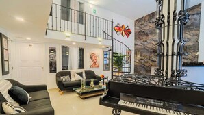 Uma sala de estar moderna com um piano de cauda, sofás pretos e uma escadaria que leva a um andar superior.