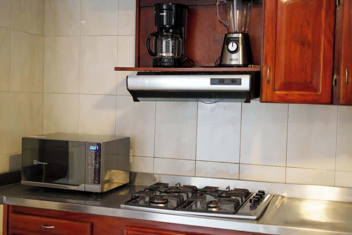 Cozinha com micro-ondas, fogão, cafeteira e liquidificador sobre uma bancada.