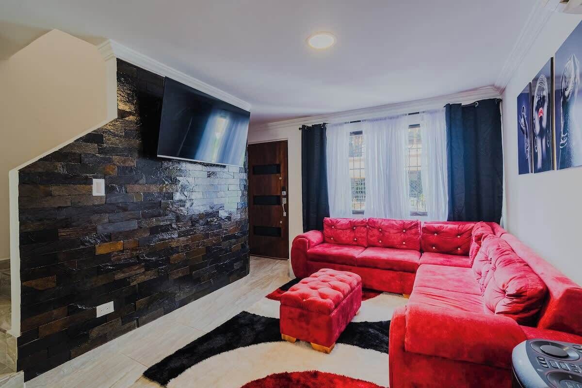 A living room with a red sofa, a black TV mounted on a stone wall, and a window with curtains.