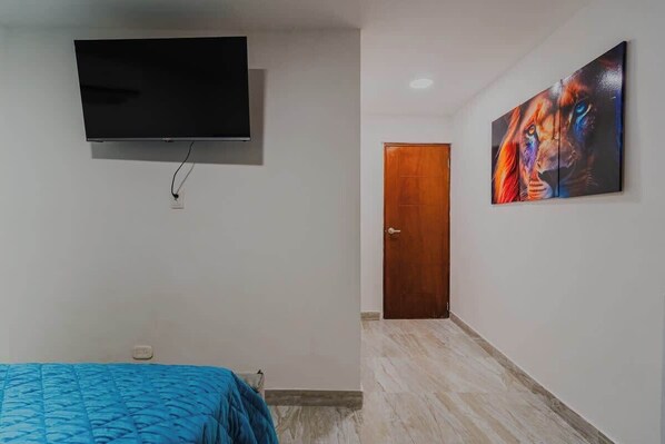 Un dormitorio con una cama, un televisor instalado en la pared y una puerta que da a otra habitación.