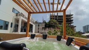 Un jacuzzi en la azotea con seis asientos negros y una estructura de pérgola de madera.
