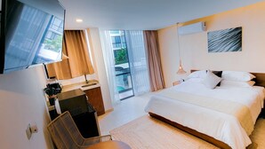 Moderni hotellihuone, jossa on suuri sänky, taulutelevisio, tietokoneella varustettu työpöytä ja parveke, jossa on verhot.
